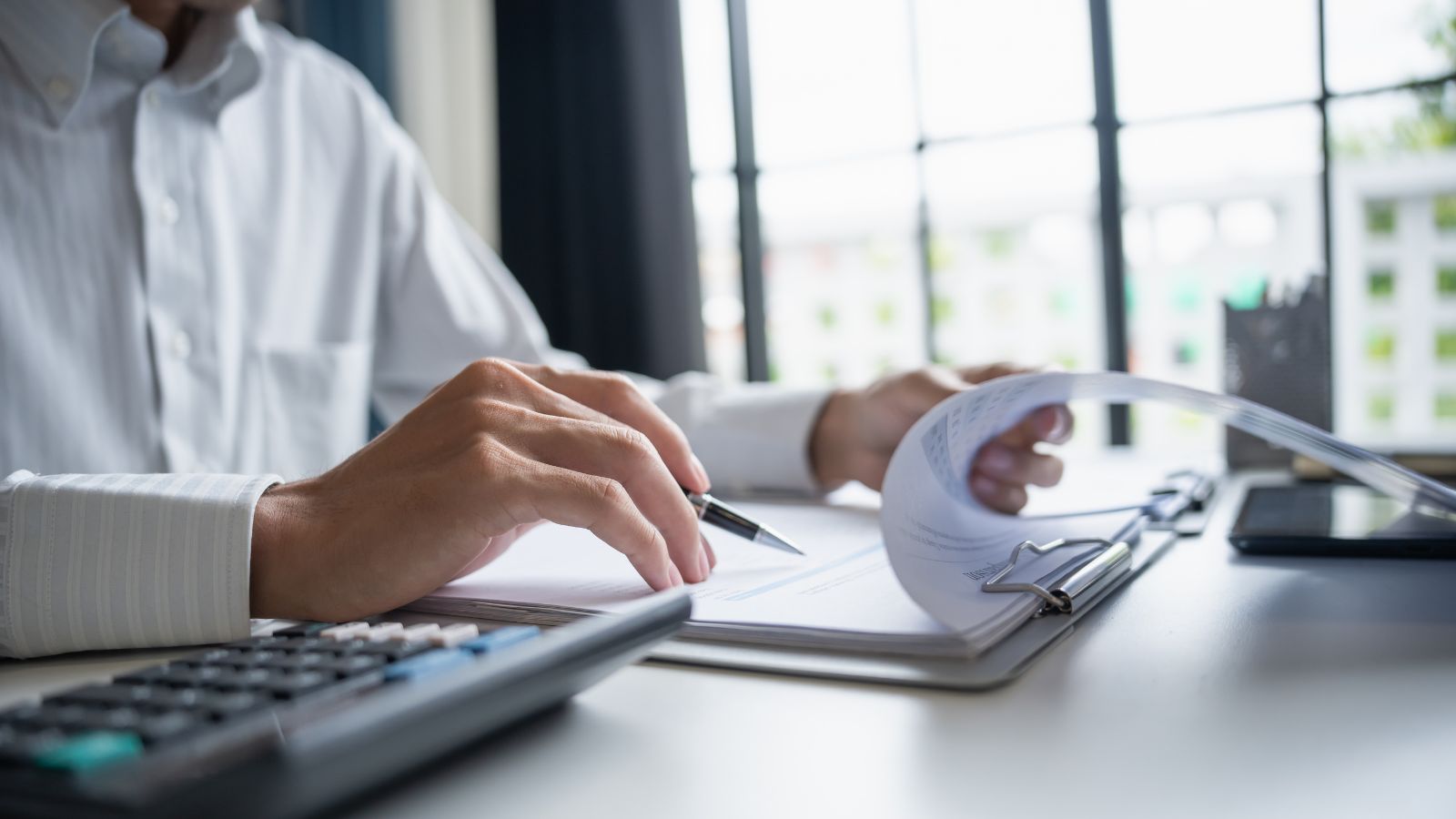 Persona revisando un balance general impreso con calculadora sobre el escritorio