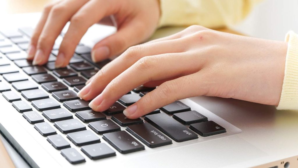 Manos escribiendo en el teclado del computador para completar en línea el trámite de eliminación de giro en el SII
