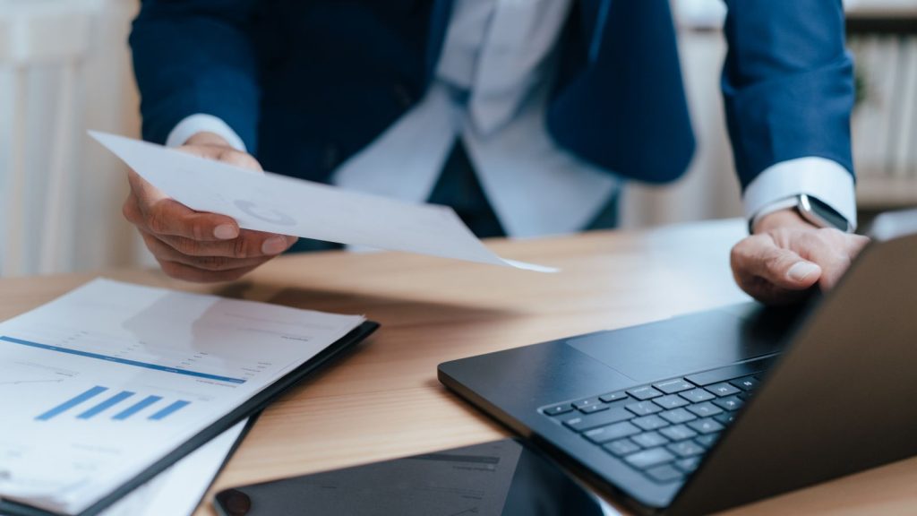 Ejecutivo revisando un reporte financiero con gráfico de barras junto a su notebook, evaluando el flujo de caja de la empresa