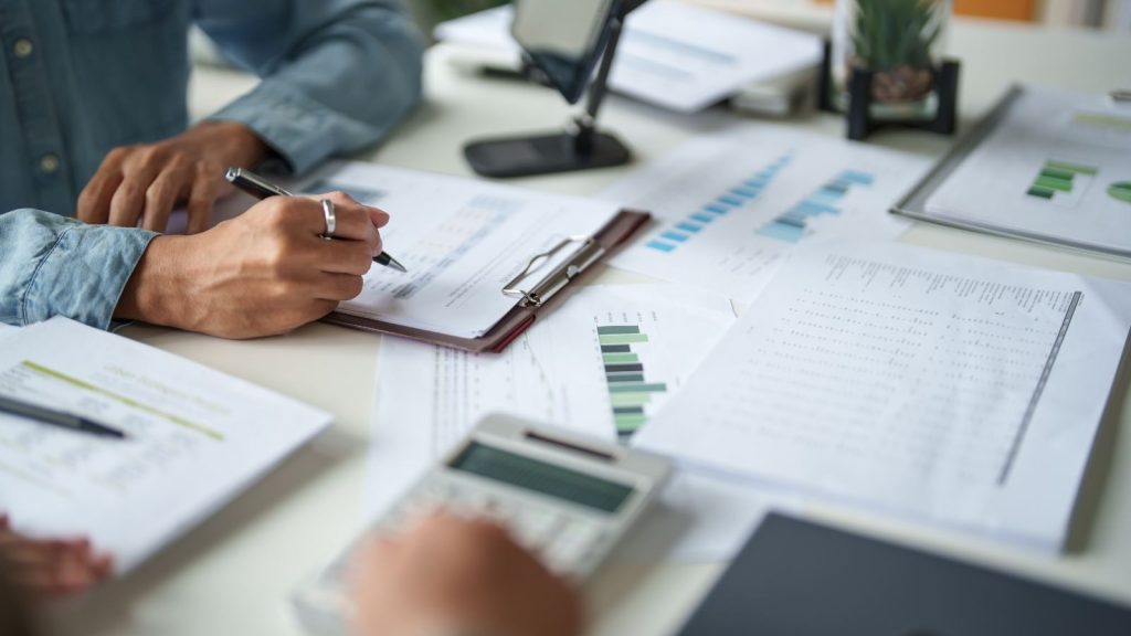 Persona tomando notas y revisando reportes financieros con calculadora para la declaración de impuestos y boletas de honorarios.