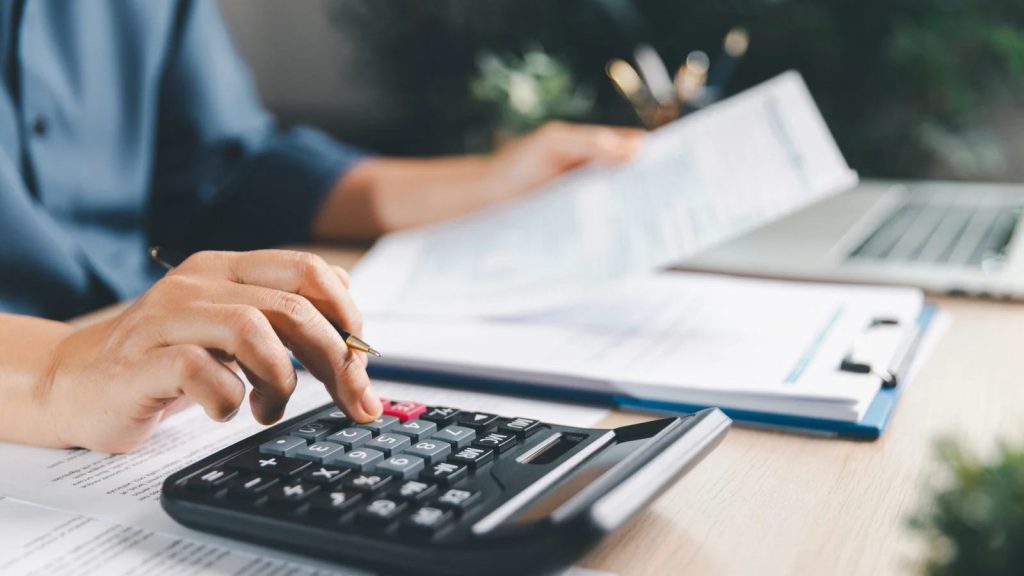 Persona calculando con calculadora el tramo de condonación de multas e intereses del SII mientras revisa documentos tributarios