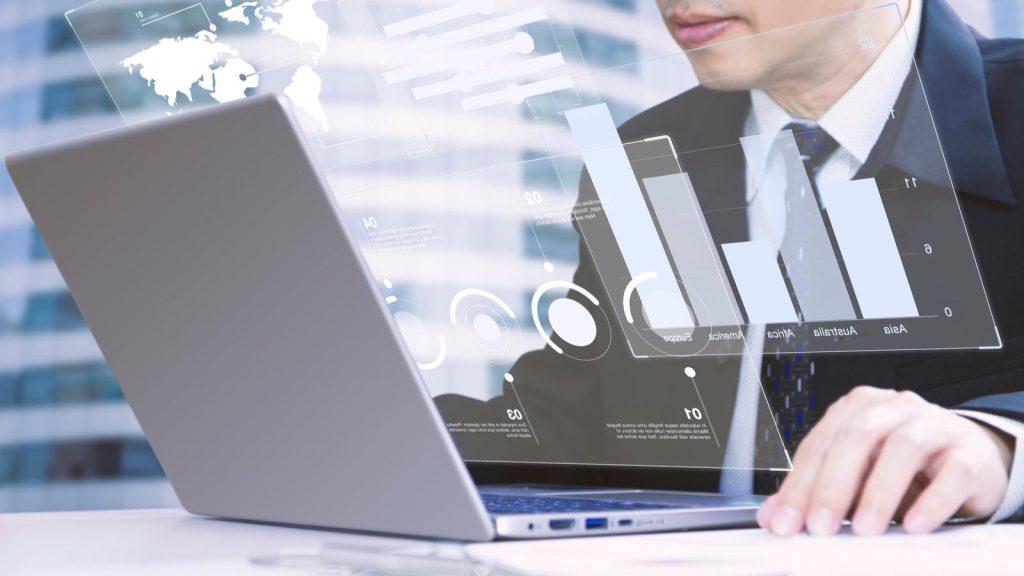 Ejecutivo frente a un laptop con gráficos de barras y datos financieros proyectados sobre la pantalla