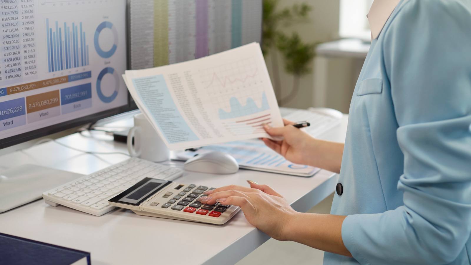 Contadora revisando informes financieros con gráficos mientras usa una calculadora frente al computador
