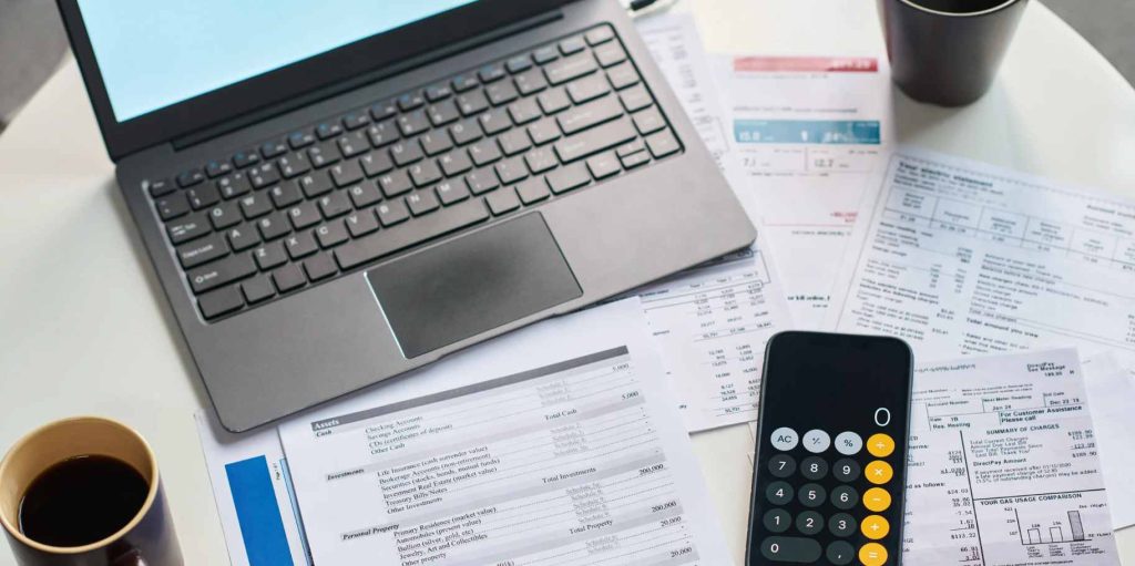 Computador portátil, calculadora en un celular y documentos financieros sobre una mesa para revisar la depreciación de activos fijos